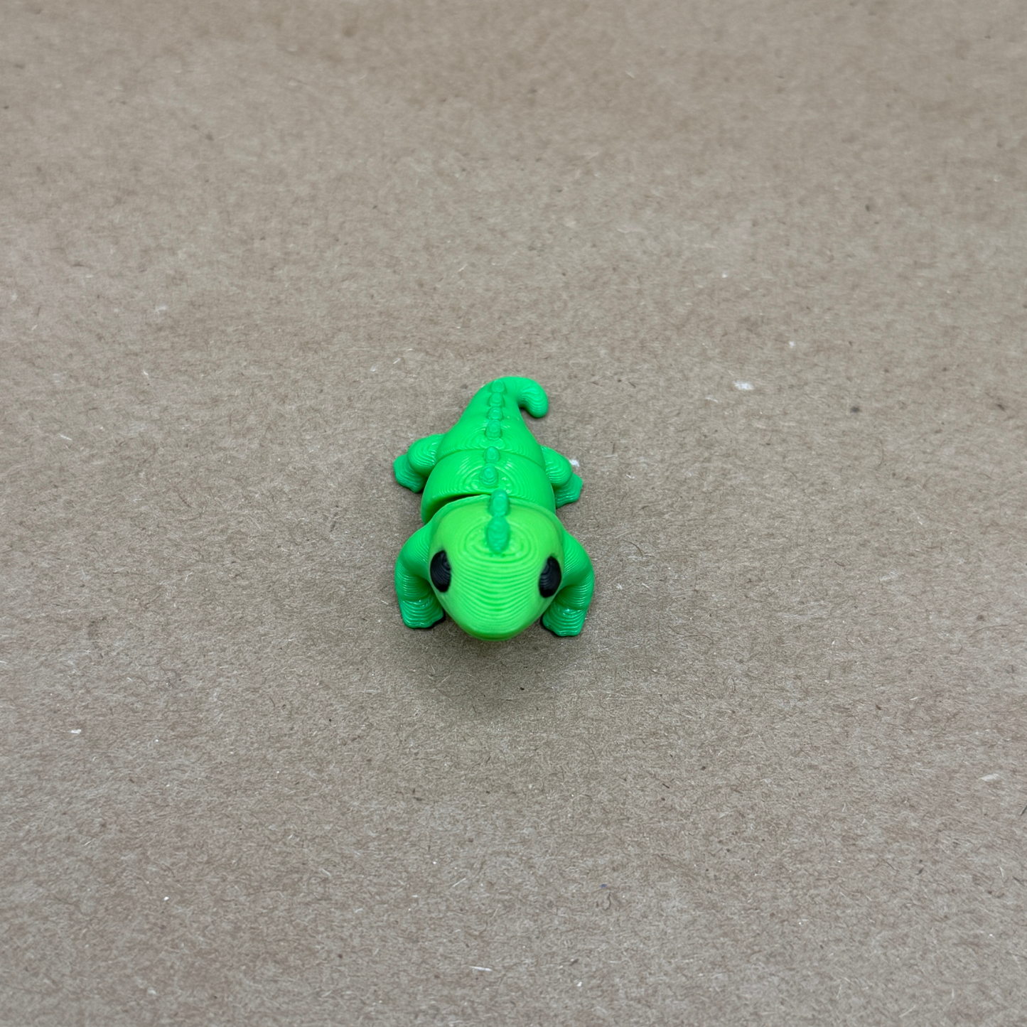 Close-up of 3D printed flexi iguana showing dorsal spines, clawed feet, and expressive eyes
