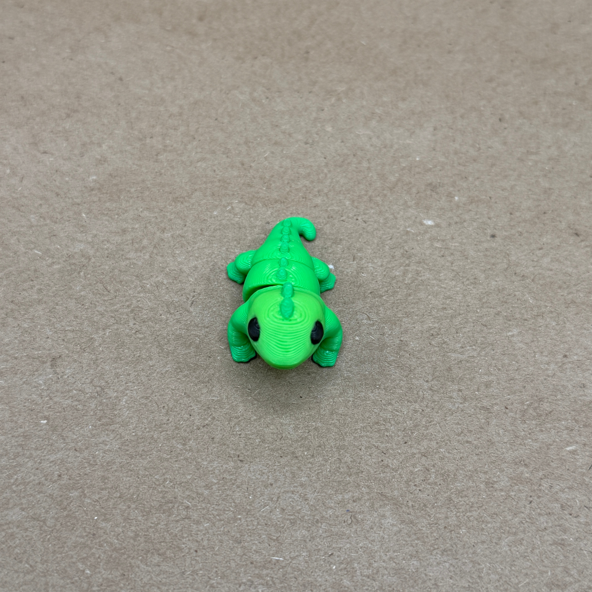 Close-up of 3D printed flexi iguana showing dorsal spines, clawed feet, and expressive eyes